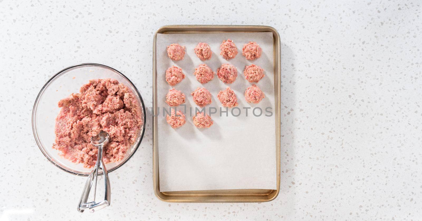 Flat lay. Scooping ground meat with dough scoop into a baking sheet lined with parchment paper to prepare oven-baked meatballs.