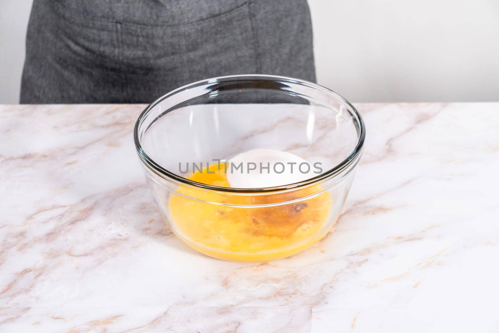 Mixing ingredients in a large glass mixing bowl to bake apple sharlotka muffin.