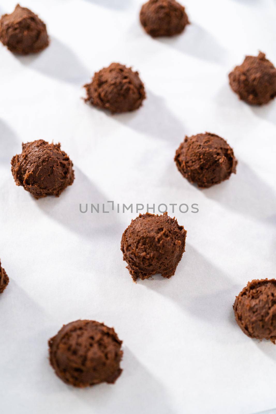 Scooping cookie dough with dough scoop into a baking sheet lined with parchment paper to bake chocolate cookies with chocolate hearts for Valentine's Day.