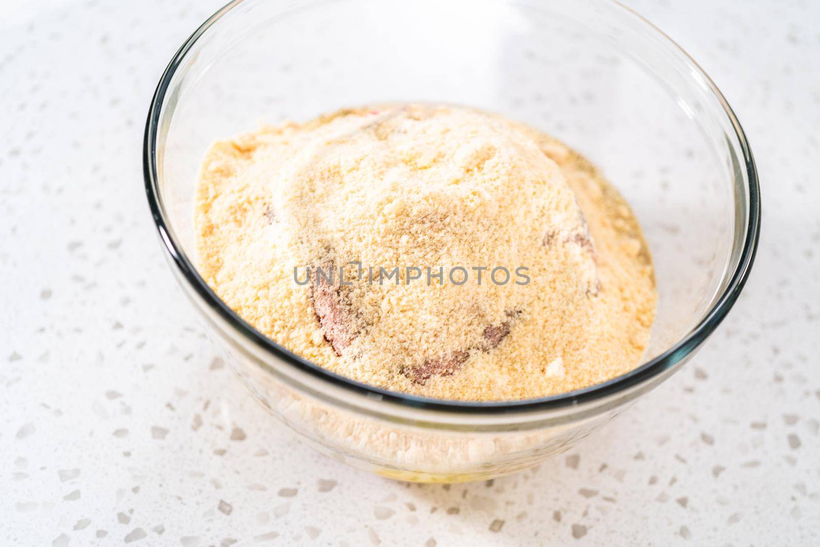 Mixing ingredients with a potatoe masher in a glass mixing bowl to prepare oven-baked meatballs.