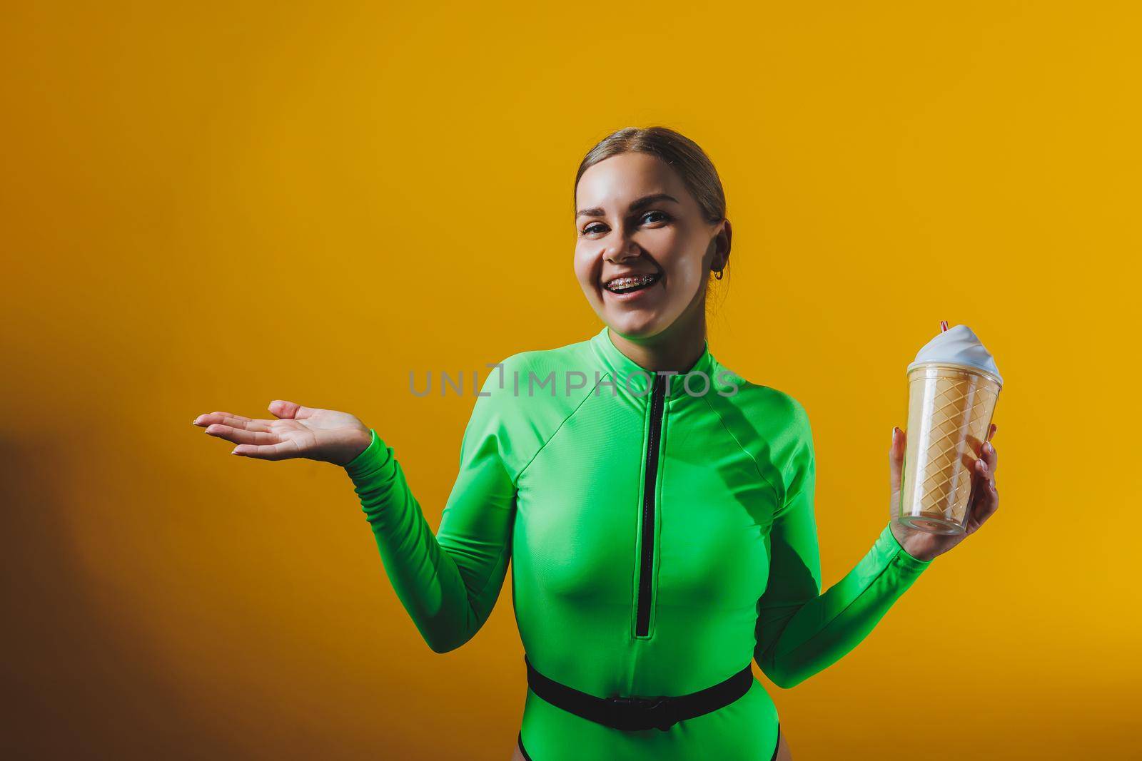 A smiling woman in a green swimsuit with a cocktail in her hands is happy about the upcoming vacation, isolated on a bright yellow background. Summer tropics travel concept.
