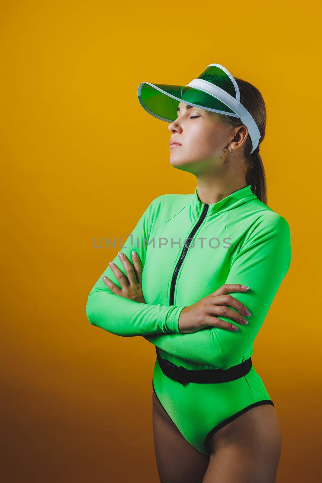 Attractive woman in bright green beach swimsuit, hat, on bright yellow background with perfect body. Isolated. Studio shot.