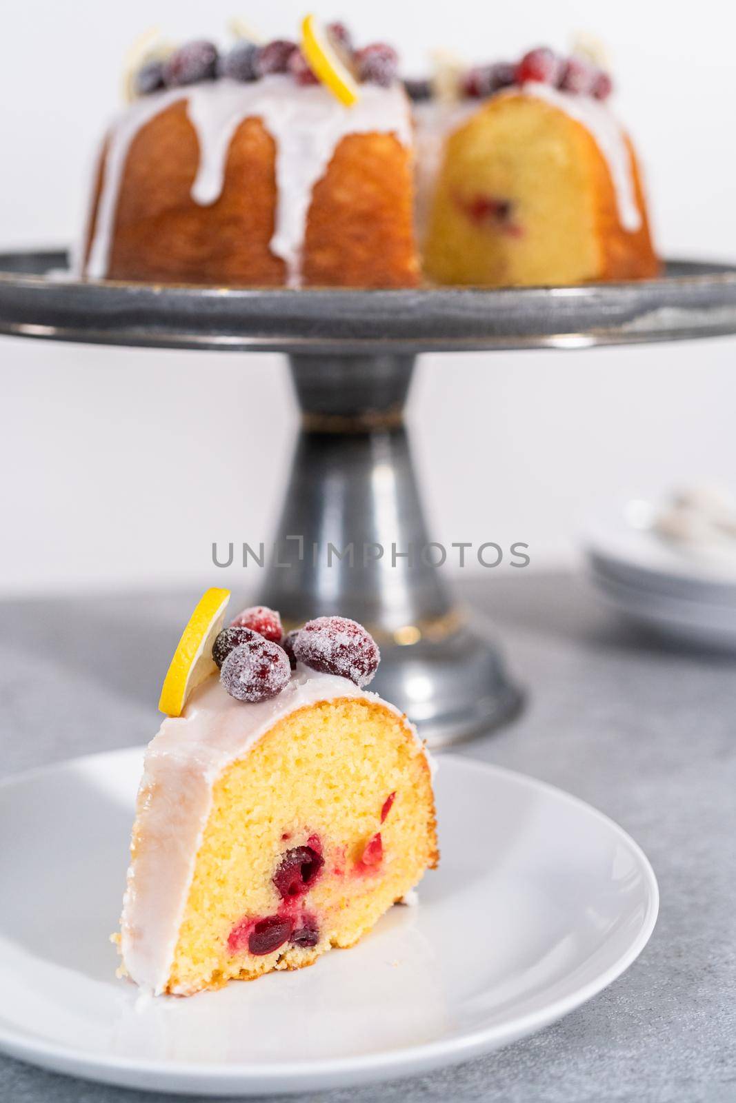 Sliced lemon cranberry bundt cake decorated with sugar cranberries and lemon wedges on a cake stand.