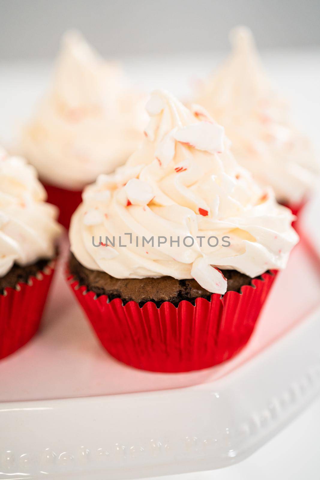 Freshly baked chocolate cupcakes with peppermint frosting and decorating with crushed peppermint candy cane candies.