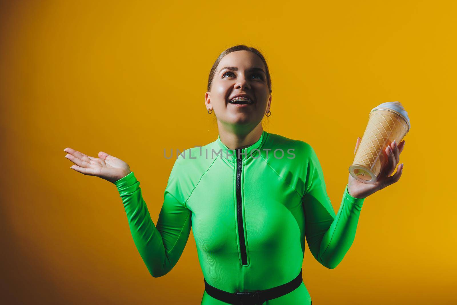 A smiling woman in a green swimsuit with a cocktail in her hands is happy about the upcoming vacation, isolated on a bright yellow background. Summer tropics travel concept.