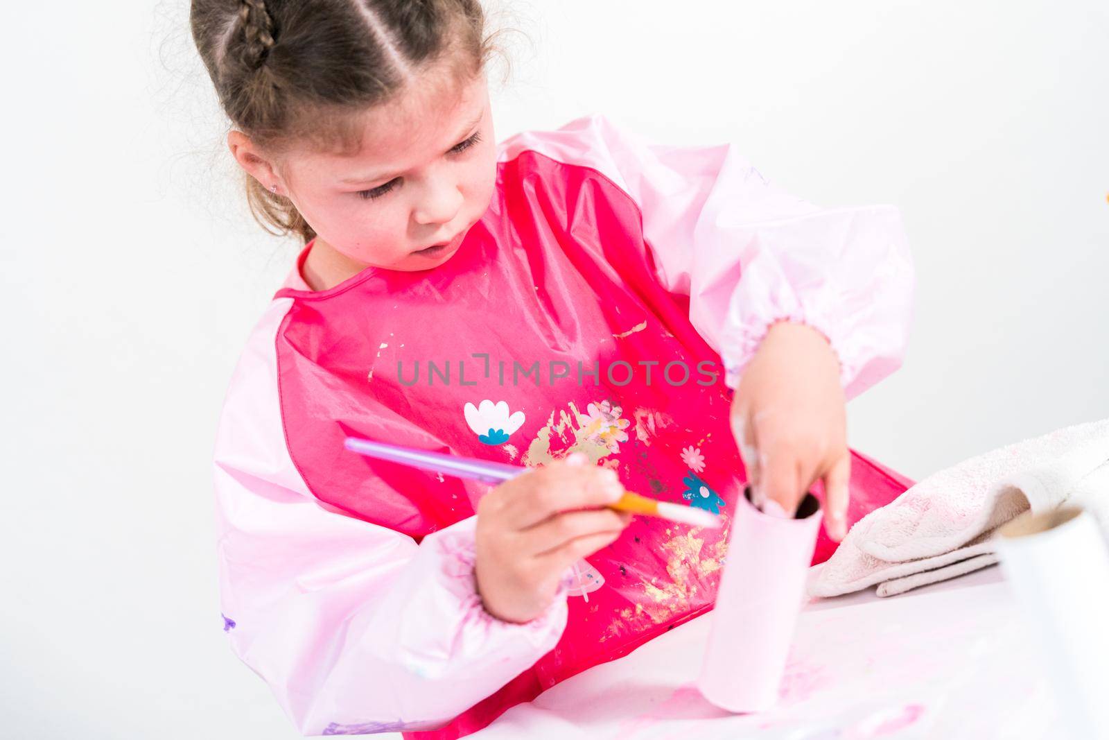 Little girl making a unicorn out of the toilet paper roll and craft paper.