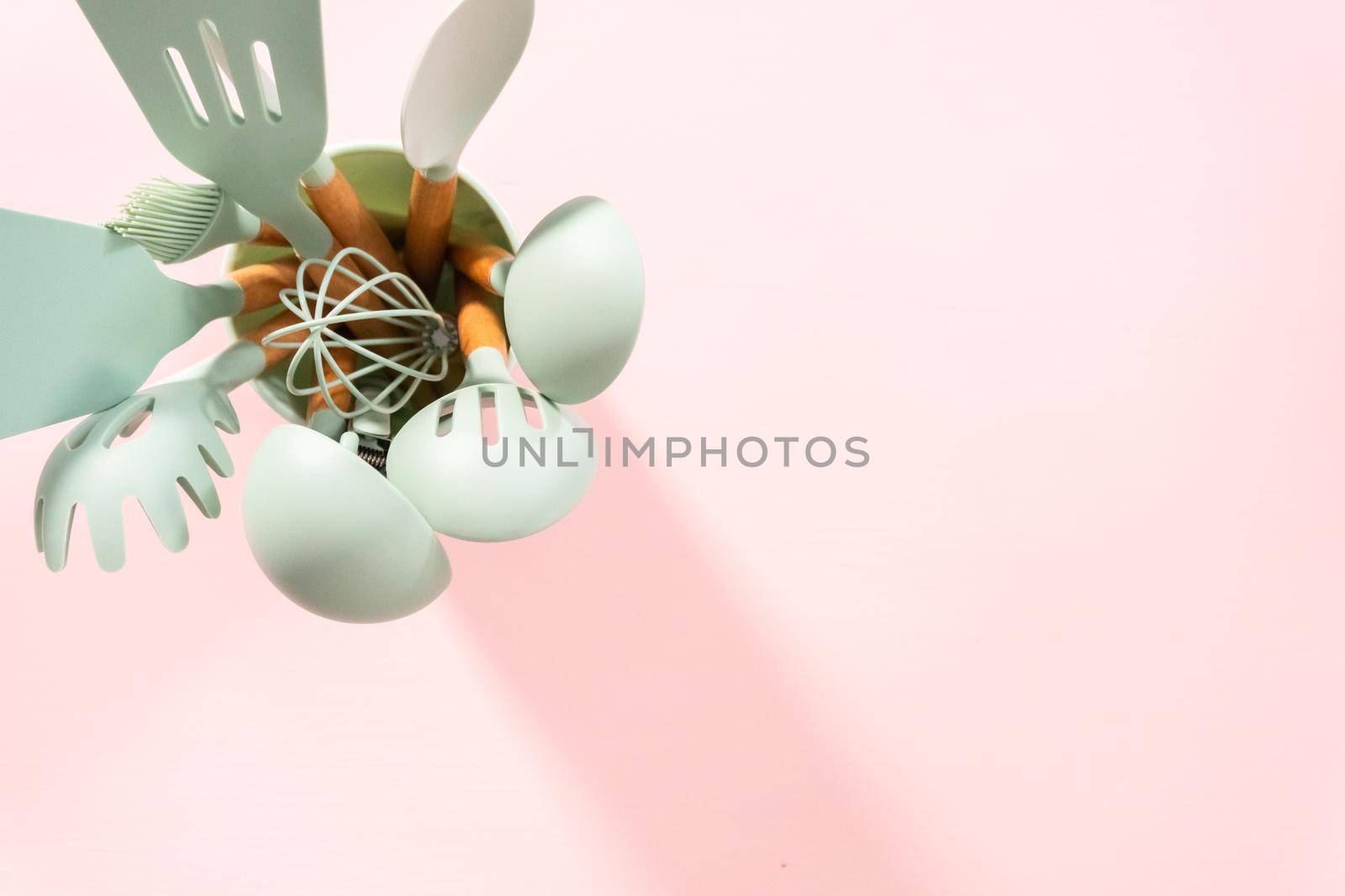 Flat lay. New blue silicone kitchen utensils with wooden handles on a pink background.