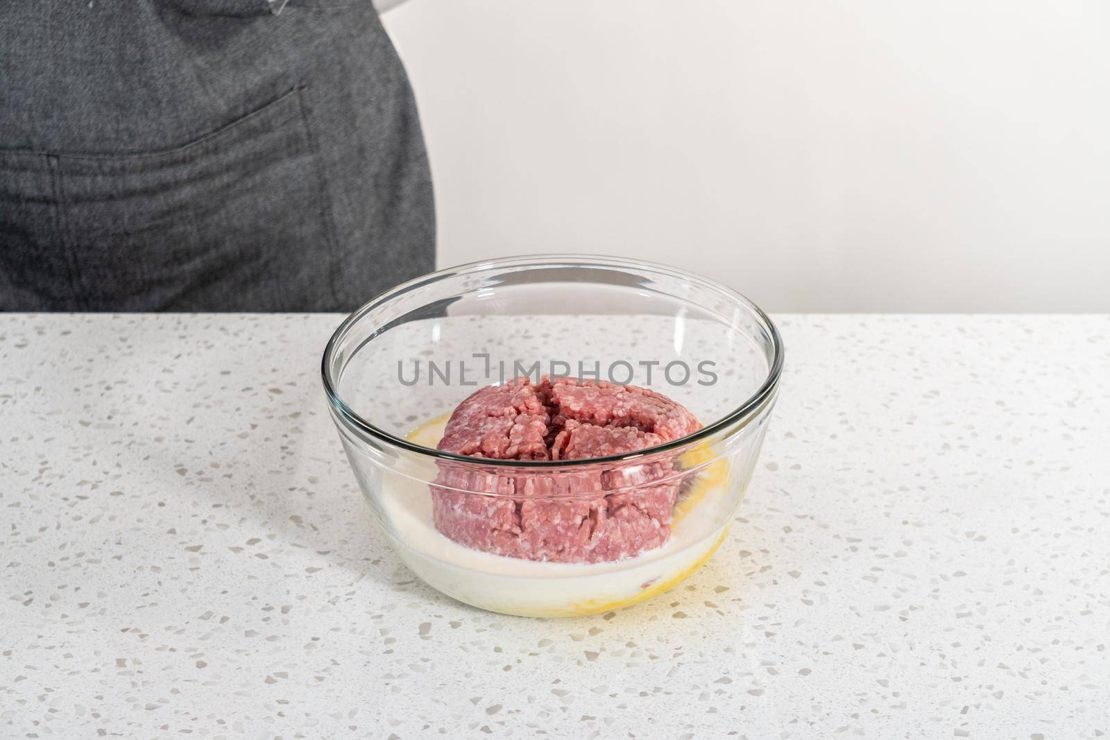 Mixing ingredients with a potatoe masher in a glass mixing bowl to prepare oven-baked meatballs.