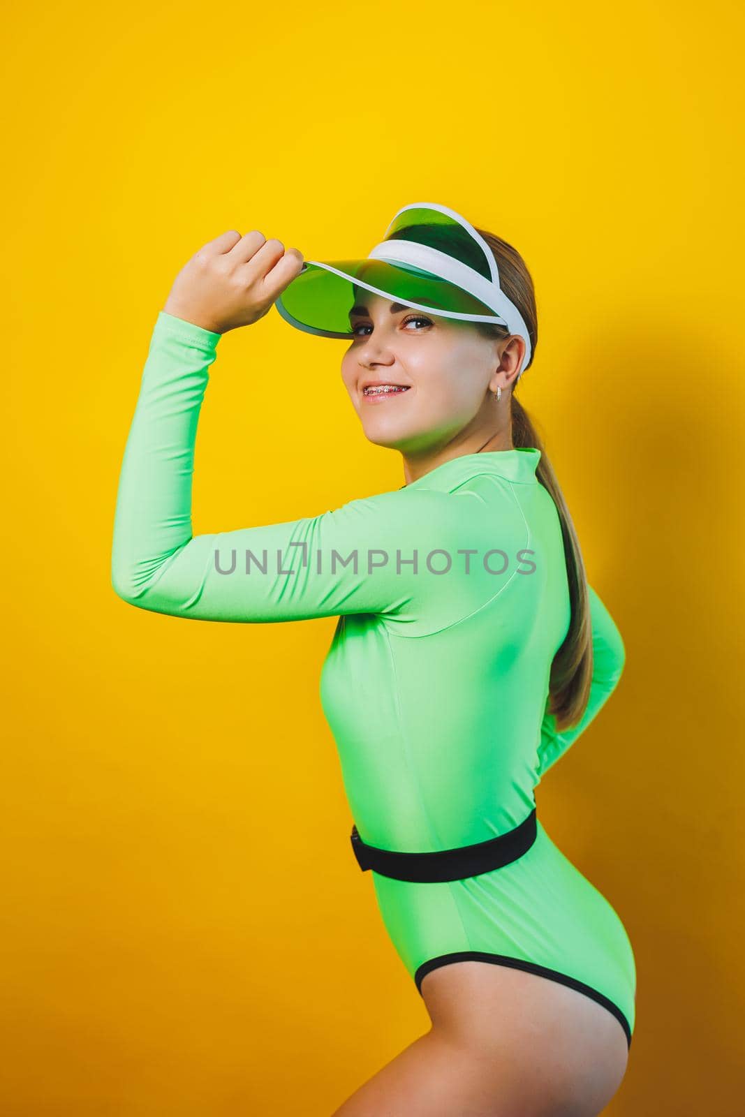 A cute slender woman in a bright green swimsuit and a sun hat on a yellow background. Summer vacation. Collection of women's swimwear