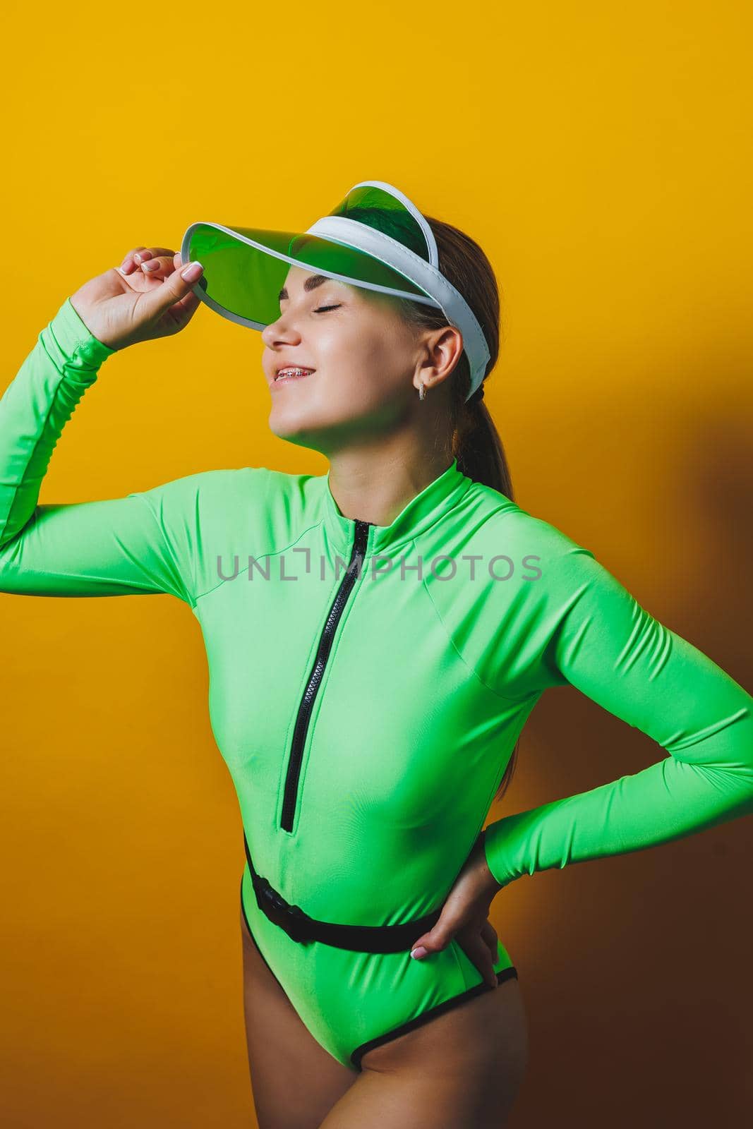Attractive woman in bright green beach swimsuit, hat, on bright yellow background with perfect body. Isolated. Studio shot.