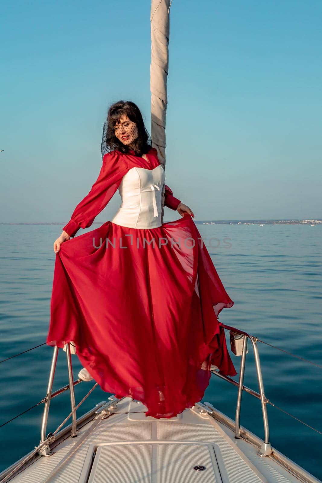 Attractive middle-aged woman in a red dress on a yacht on a summer day. Luxury summer adventure, outdoor activities