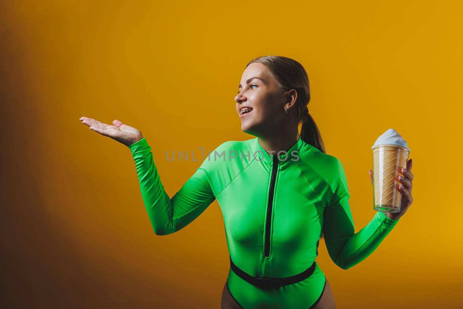 A smiling woman in a green swimsuit with a cocktail in her hands is happy about the upcoming vacation, isolated on a bright yellow background. Summer tropics travel concept.
