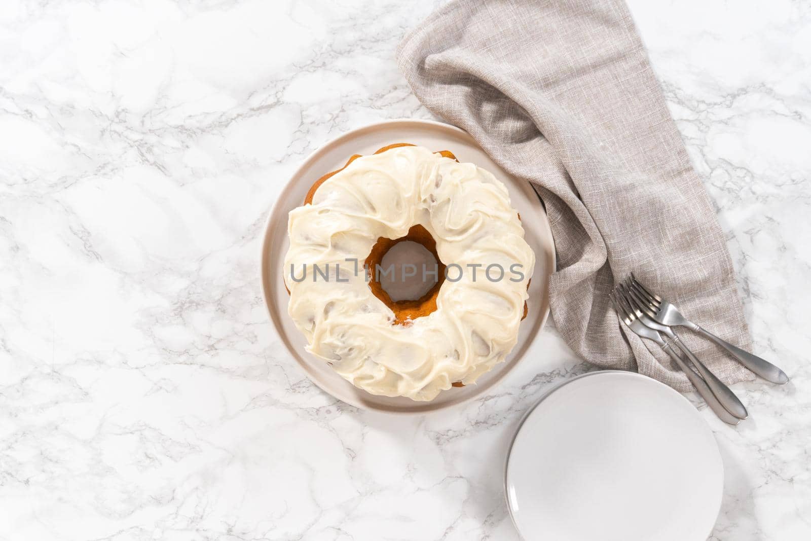 Flat lay. Freshly baked pumpkin bunt cake with cream cheese frosting on the kitchen counter.