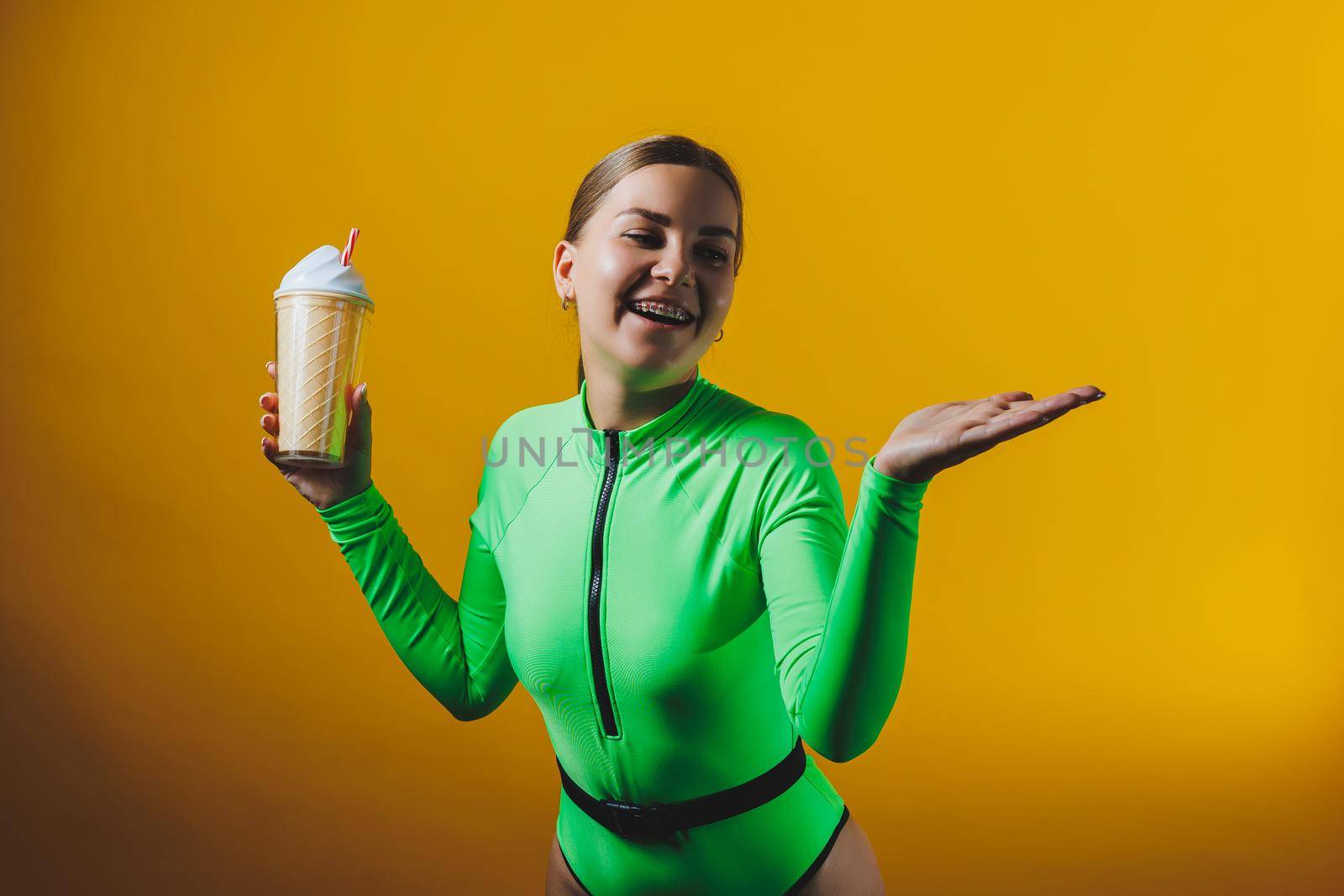 A smiling woman in a green swimsuit with a cocktail in her hands is happy about the upcoming vacation, isolated on a bright yellow background. Summer tropics travel concept.