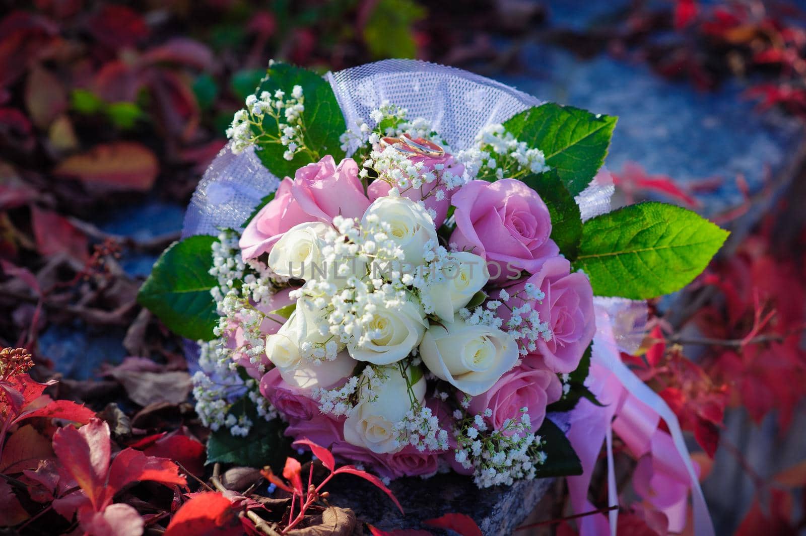 Bridal wedding bouquet of flowers with golden rings. Wedding bouquet of pink and white roses lying on a grass by Andrii_Ko