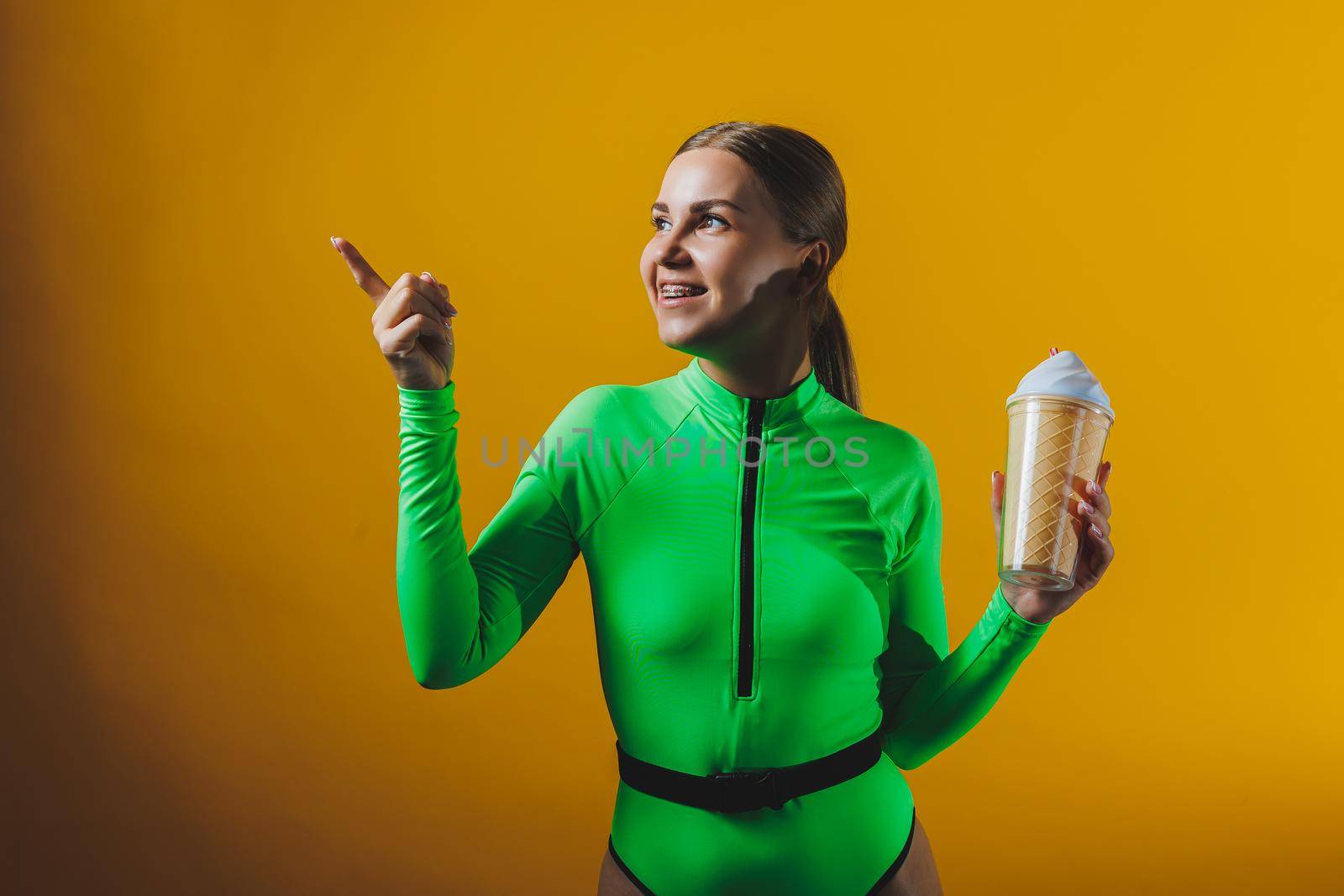 A smiling woman in a green swimsuit with a cocktail in her hands is happy about the upcoming vacation, isolated on a bright yellow background. Summer tropics travel concept.