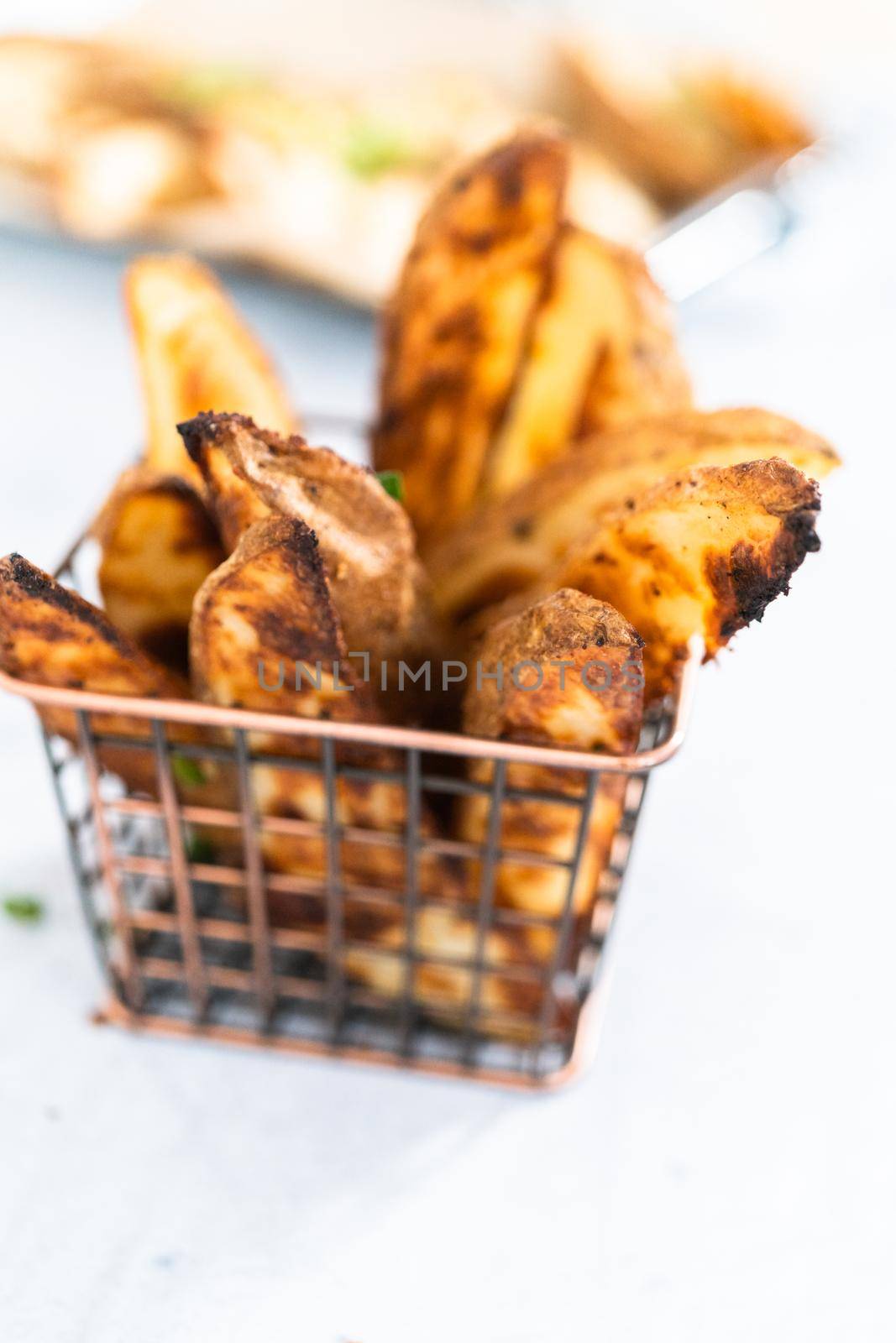 Freshly baked potato wedges with spices in a wire basket.