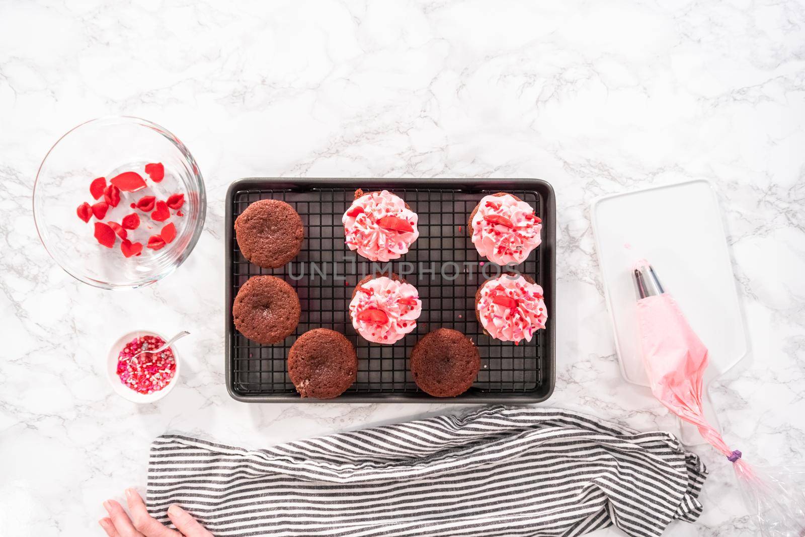 Flat lay. Frosting red velvet cupcakes with pink Italian buttercream frosting.