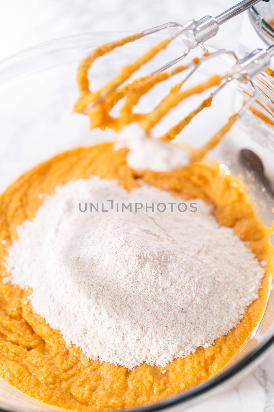 Mixing ingredients in a large glass mixing bowl to bake pumpkin bunt cake.