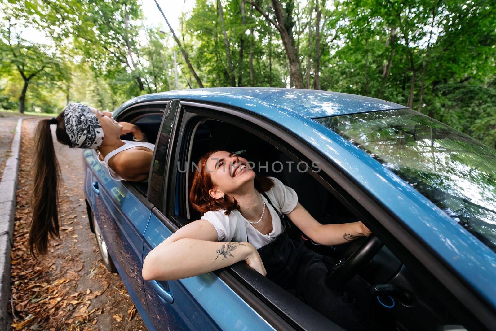 Two attractive young girlfriends fool around and laughing together in a car on a sunny day.