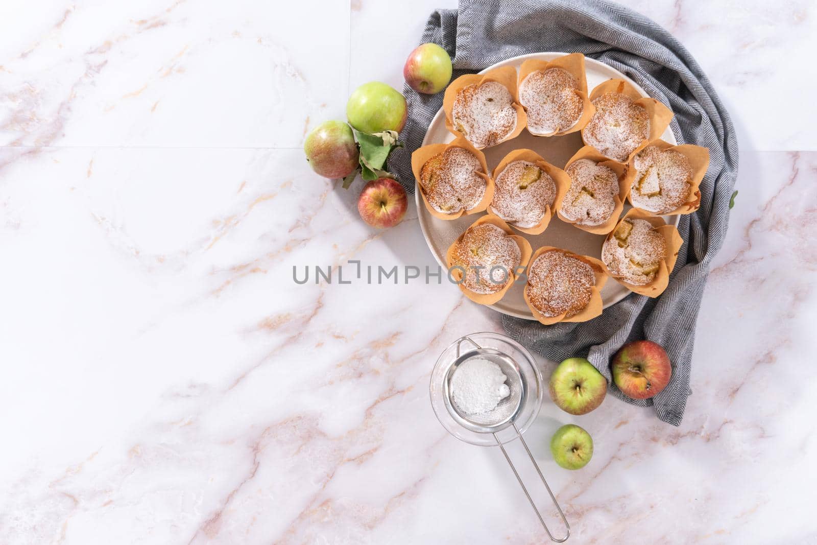Flat lay. Freshly baked apple sharlotka muffin dusted with powdered sugar on a white plate.