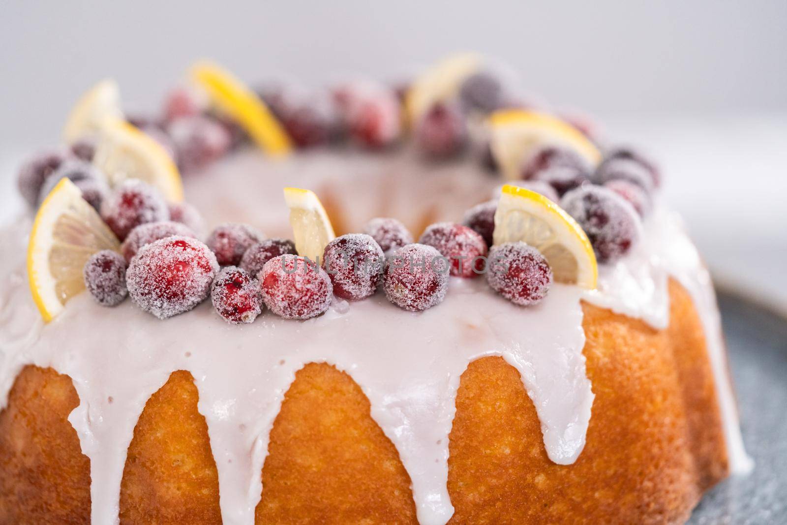 Lemon cranberry bundt cake decorated with sugar cranberries and lemon wedges on a cake stand.