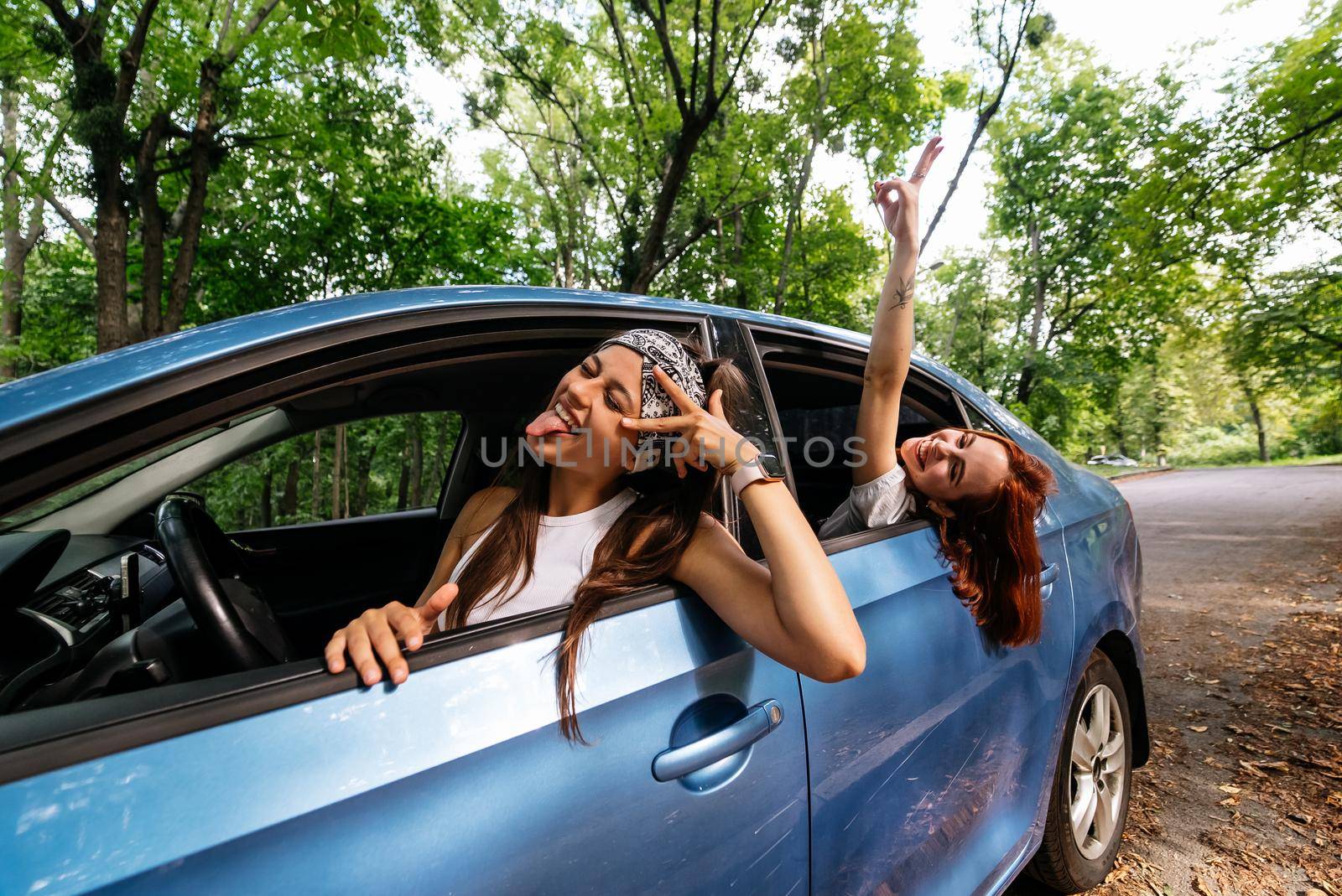 Two attractive young girlfriends fool around and laughing together in a car on a sunny day.