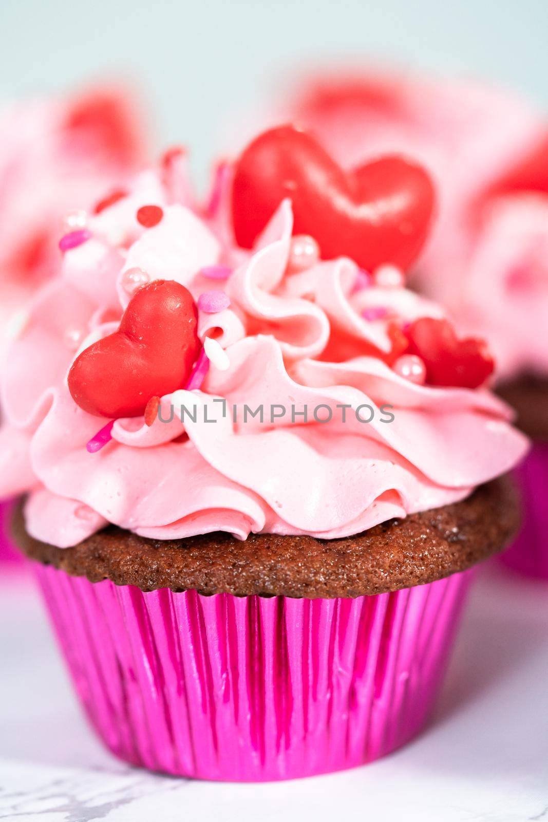 Red velvet cupcakes with pink Italian buttercream frosting and decorates with heart and kiss shaped red chocolates.