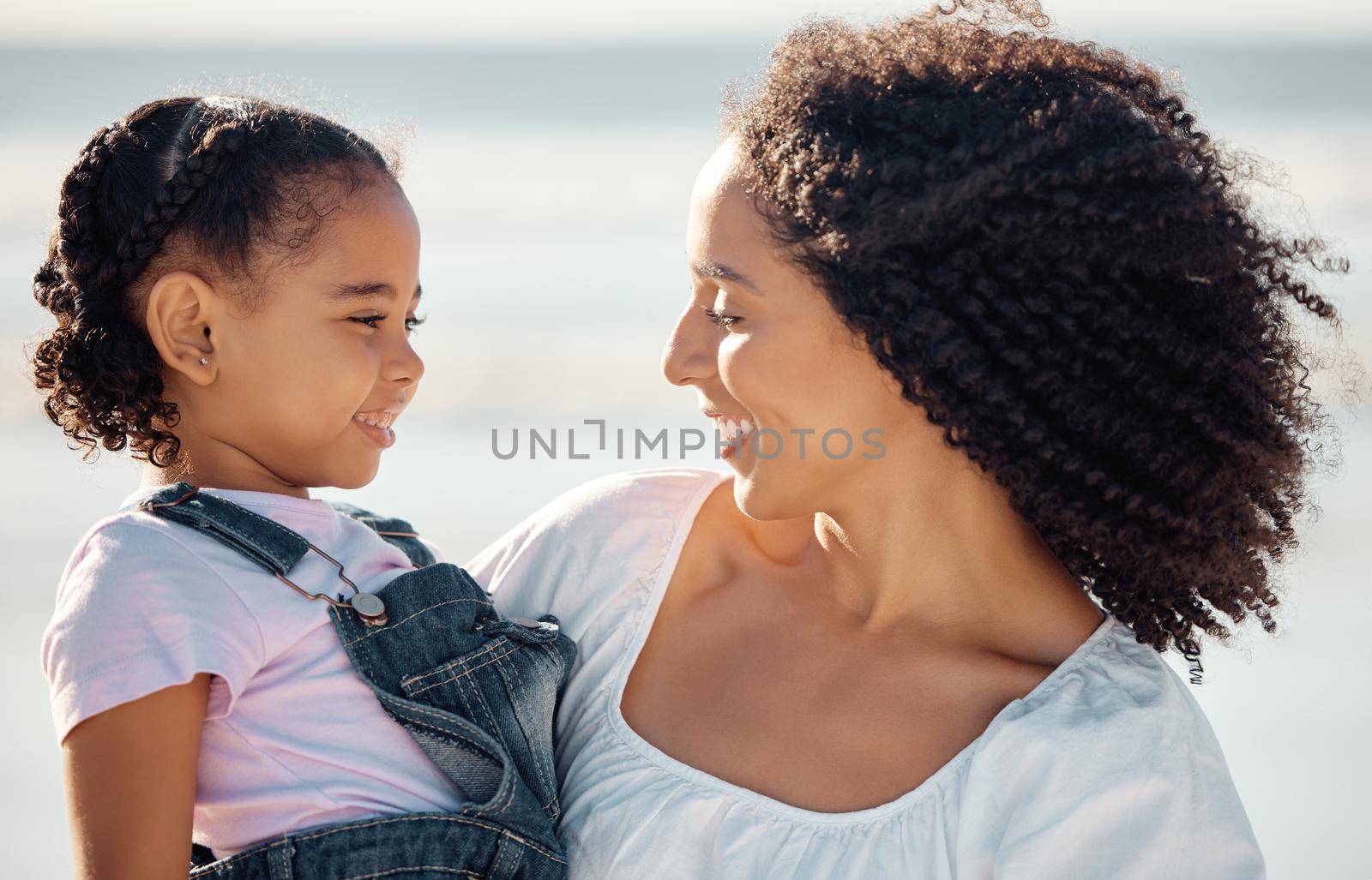 Mom with child at beach smile, make eye contact and black family happiness. Black woman with girl, happy spend time as mother and daughter, on family holiday or vacation by the ocean in Brazil.