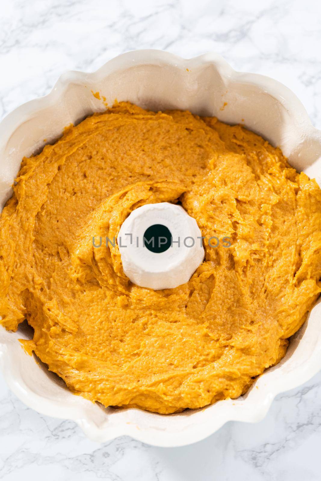 Pouring cake batter into a greased bunt cake pan to bake pumpkin bunt cake.