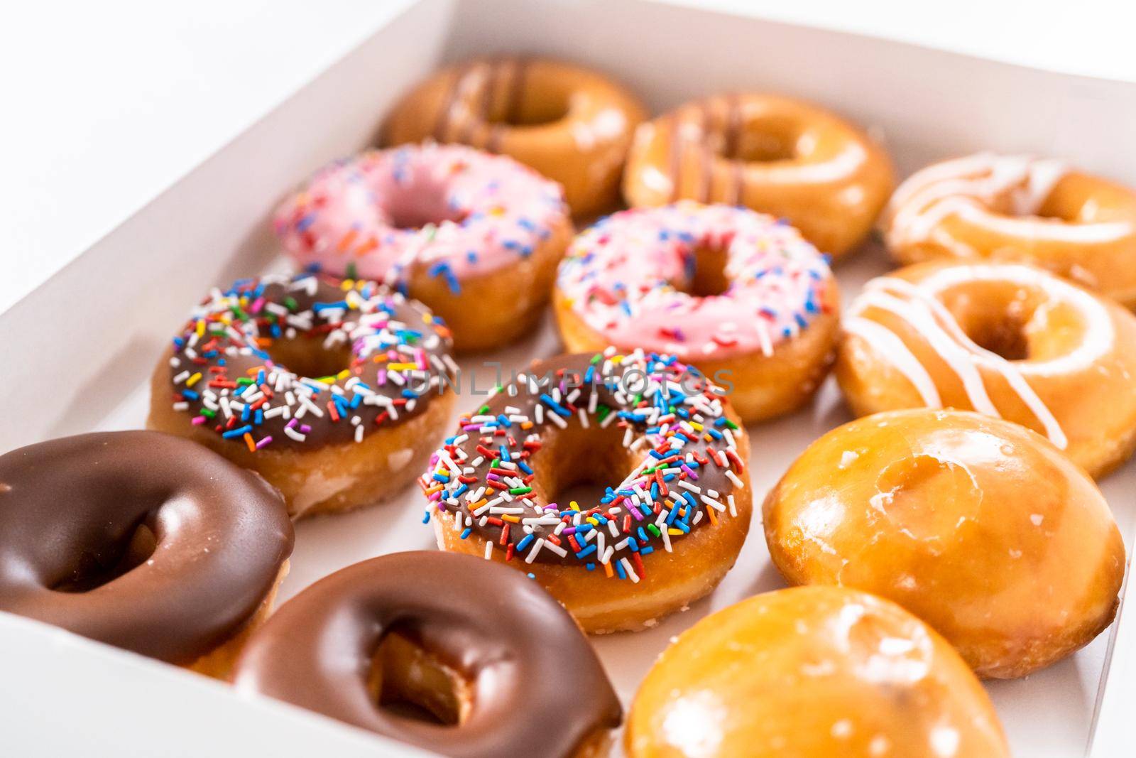 Variety of store-bought doughnuts in a white paper box.