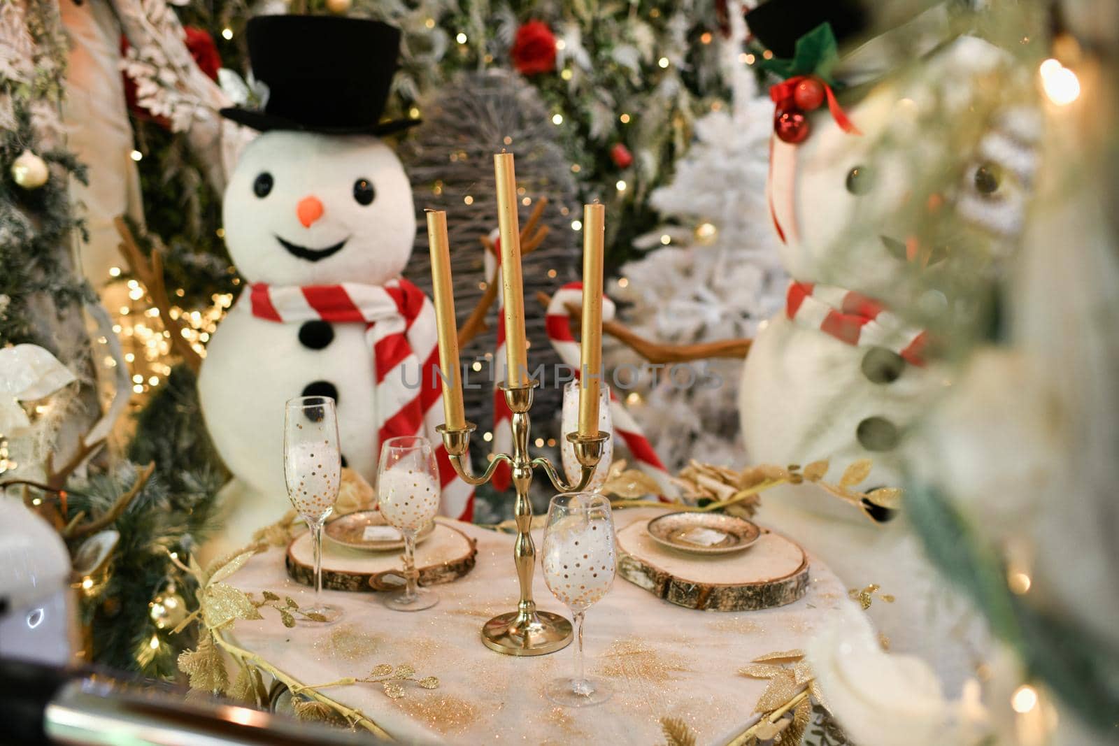 Snowmen sit at the Christmas table with the candles