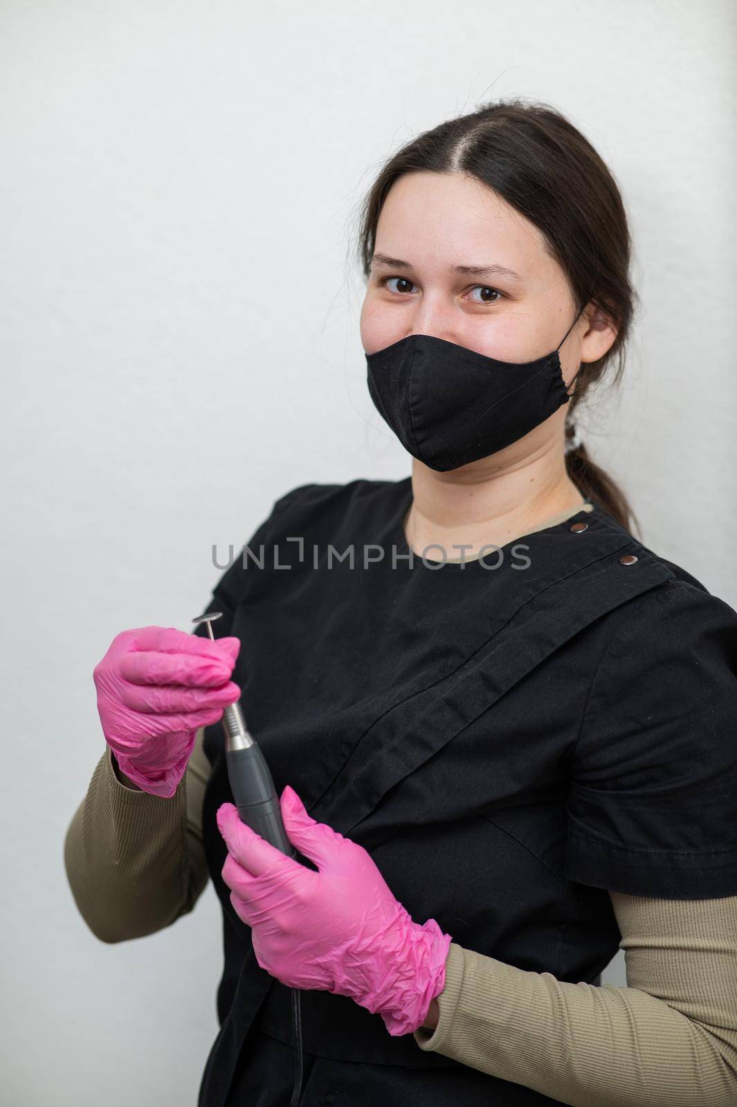 The pedicure master stands against the background of a white wall and holds an apparatus with an abrasive disc. by mrwed54