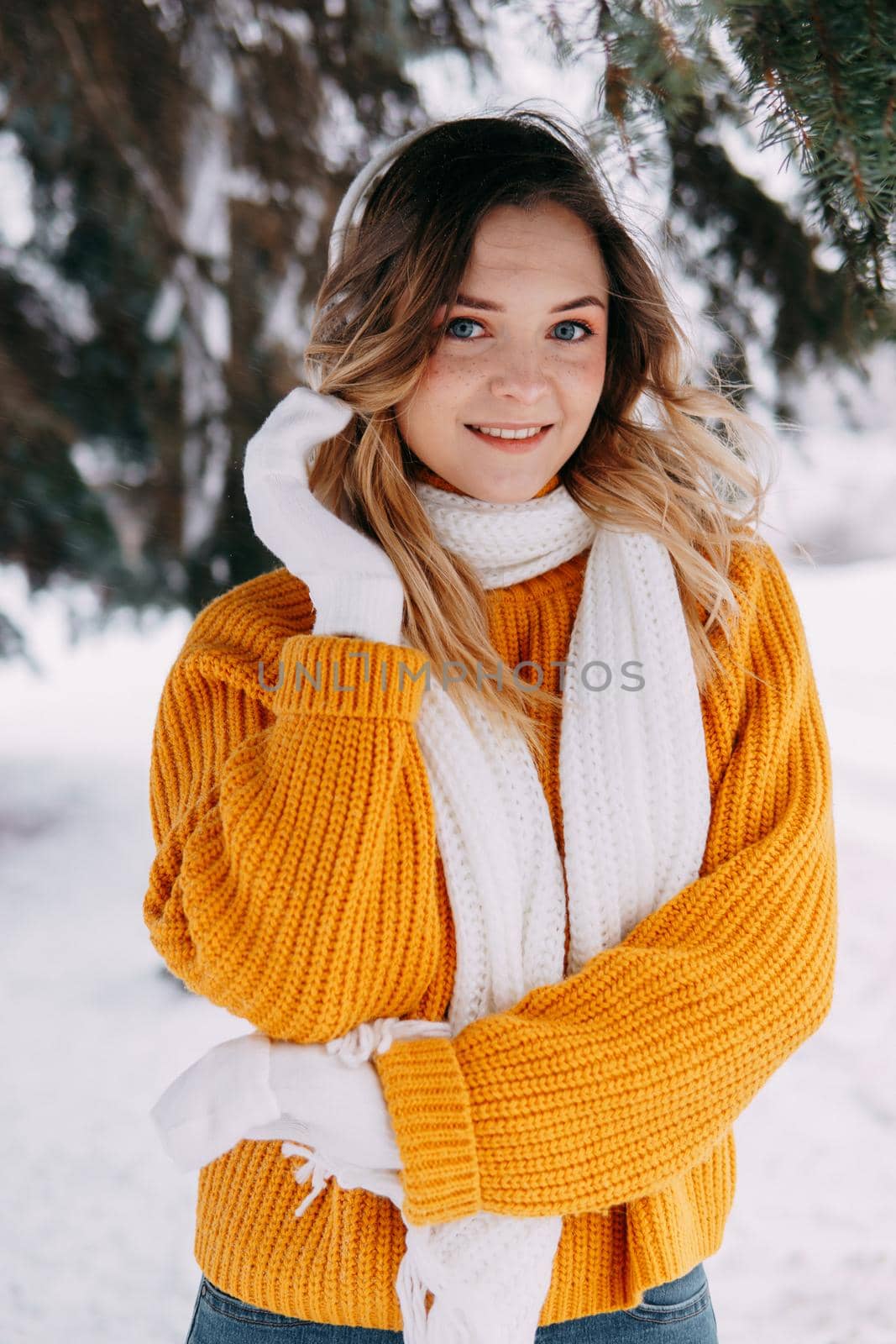 Teen blonde in a yellow sweater outside in winter. A teenage girl on a walk in winter clothes in a snowy forest.