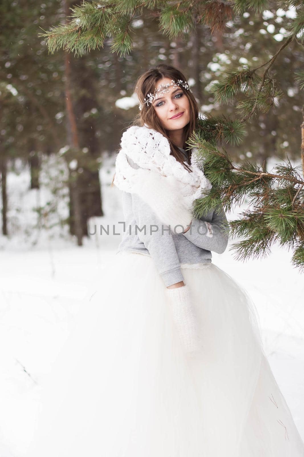 Beautiful bride in a white dress with a bouquet in a snow-covered winter forest. Portrait of the bride in nature.