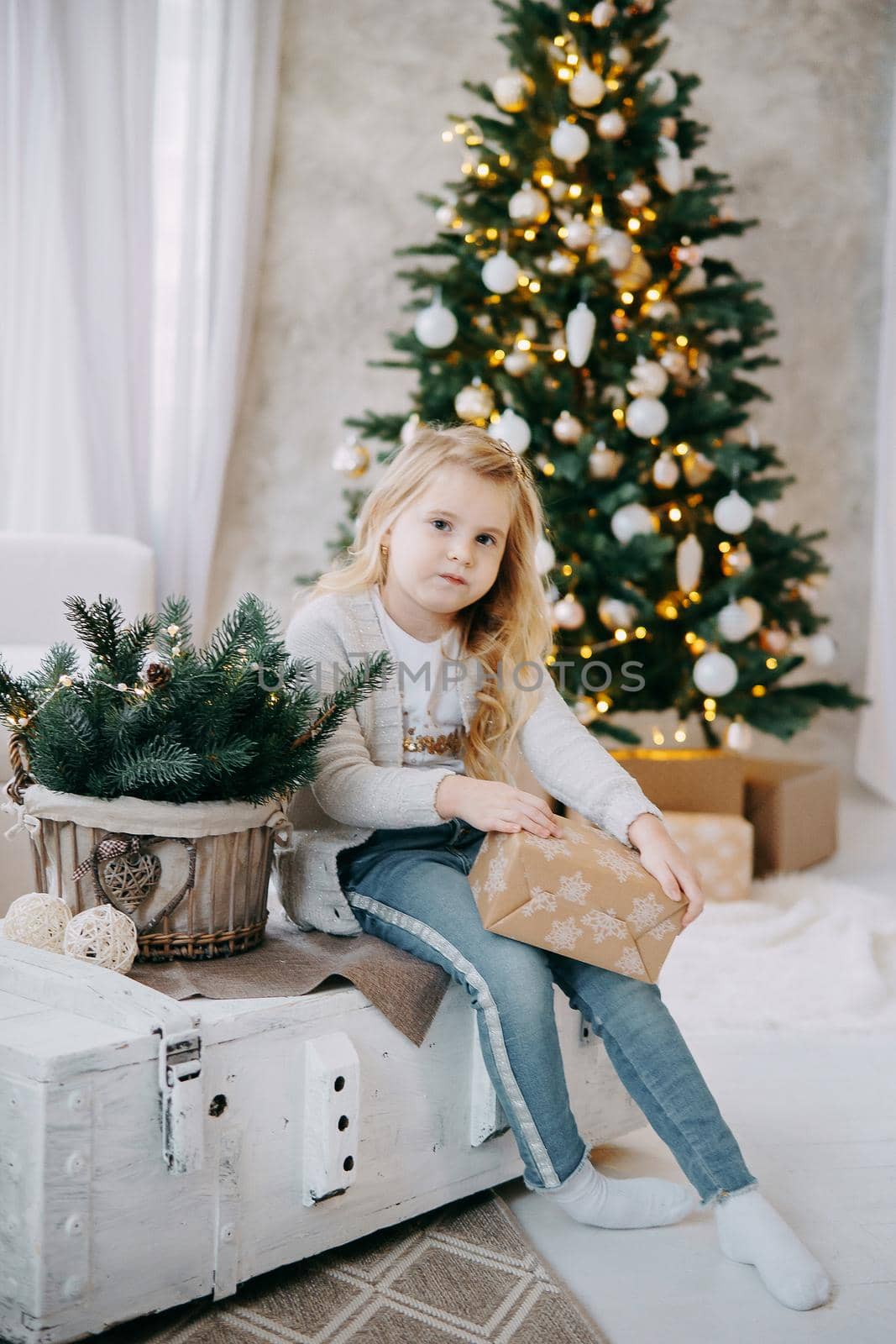 A blonde girl with a Christmas gift in her hands, on the background of a Christmas tree.The concept of New Year's decor and New Year's holidays.
