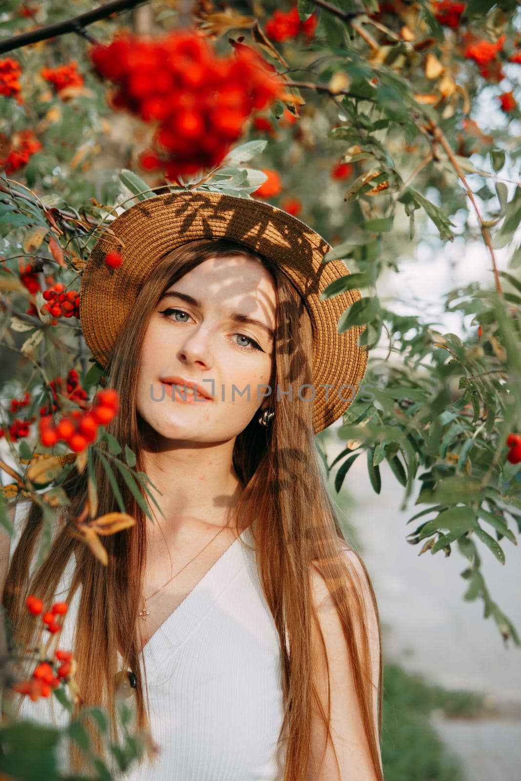 A beautiful blonde girl in a hat with long hair, on a walk in the autumn season. Portrait of a woman at a rowan tree.