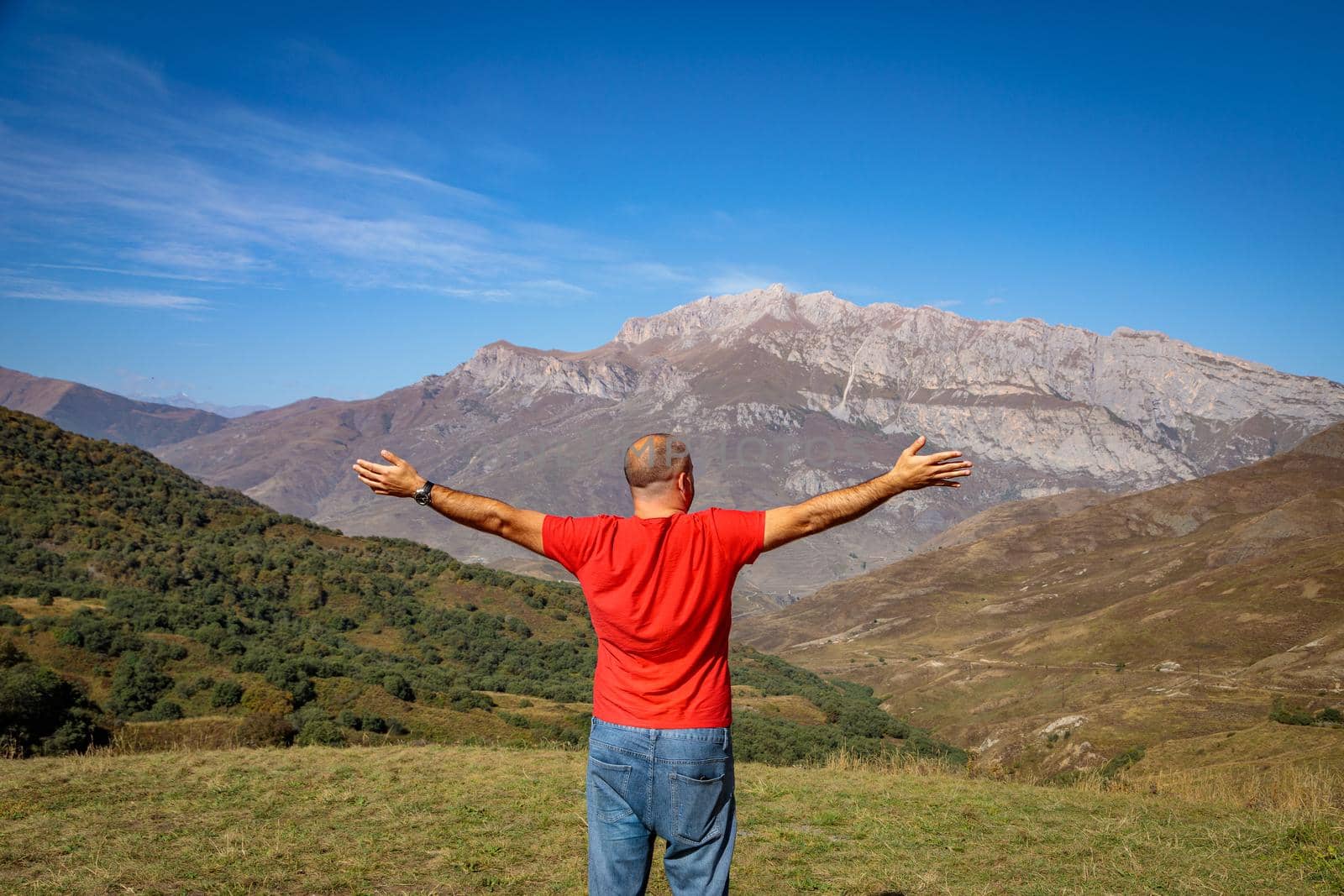 A man stands on top of a mountain with his arms outstretched