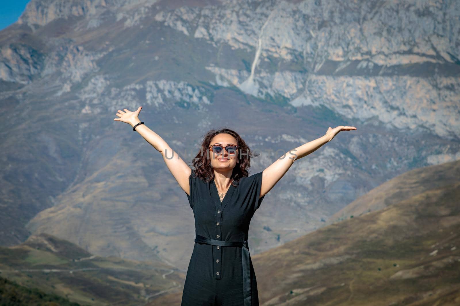 A young woman stands on top of a mountain with her arms outstretched