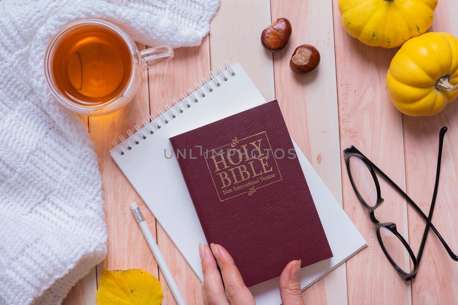 Holy Bible in female hand and autumn cozy top view on wooden background. Bible study autumn concept by ssvimaliss