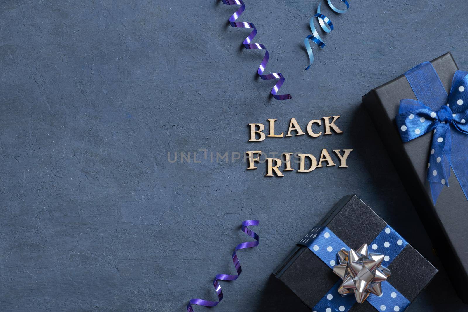 Black Friday text with gifts and holiday tinsel flat lay flat lay on dark cement background copy space. Top view.