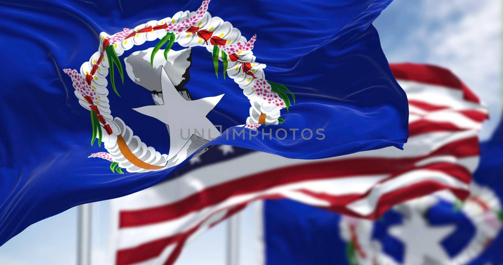 Flags of Northern Mariana Islands waving in the wind with the US flag on a clear day. The Northern Mariana Islands are an unincorporated territory and commonwealth of the United States