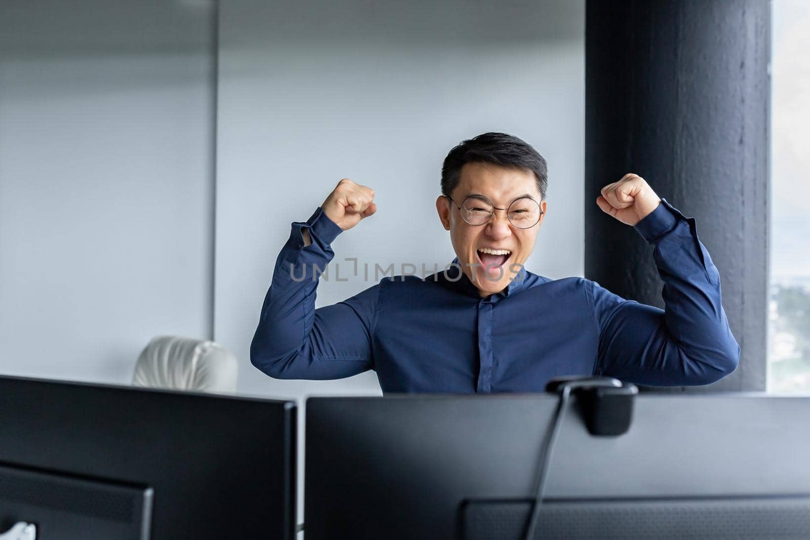 Happy Asian boss leader of programmer team, looking at computer screen and happy, celebrating victory, completed project, and submitted completed program, businessman entrepreneur holding hands up.