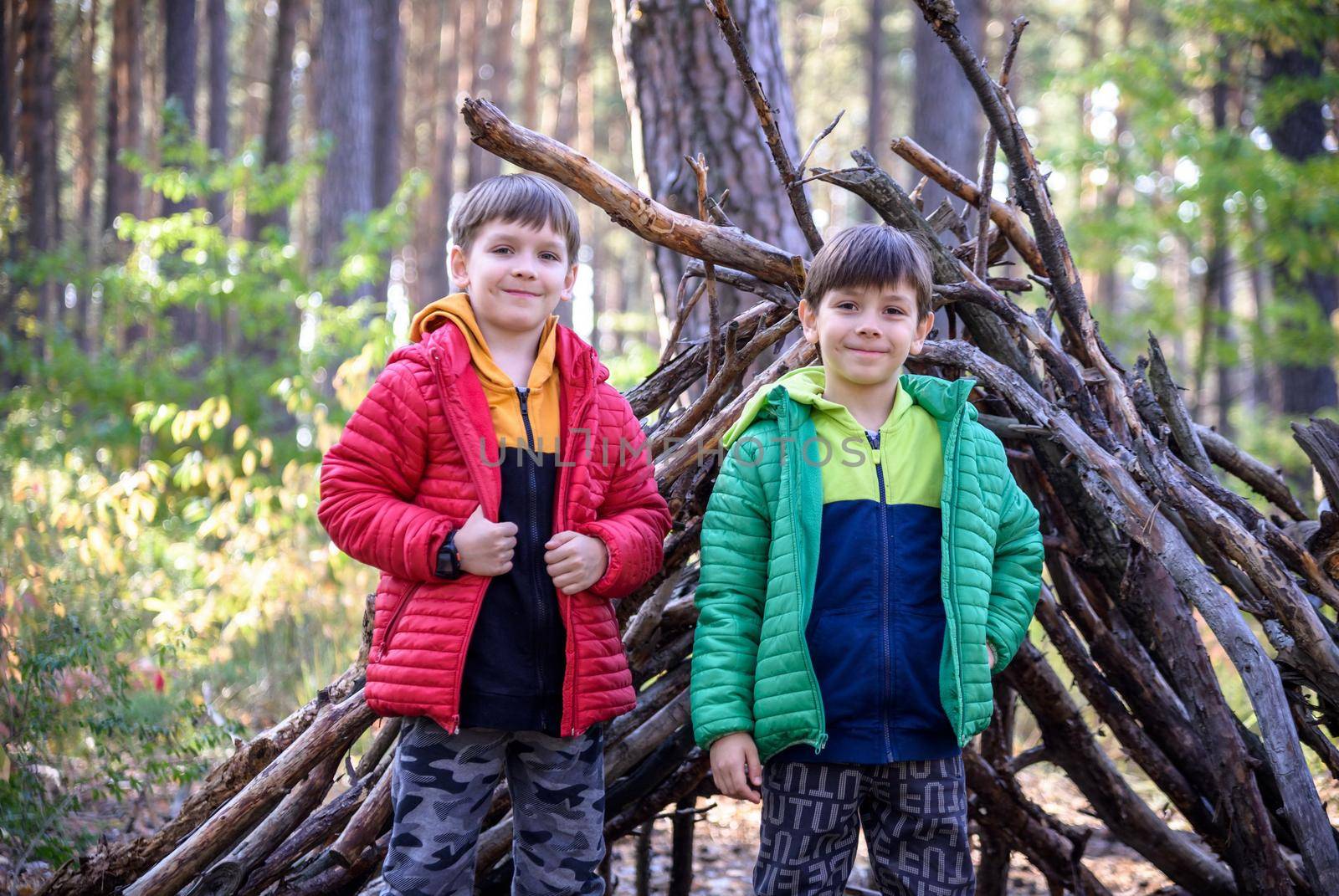 Two sibling brothers boys In the spring or autumn pine forest plays built a hut of sticks.