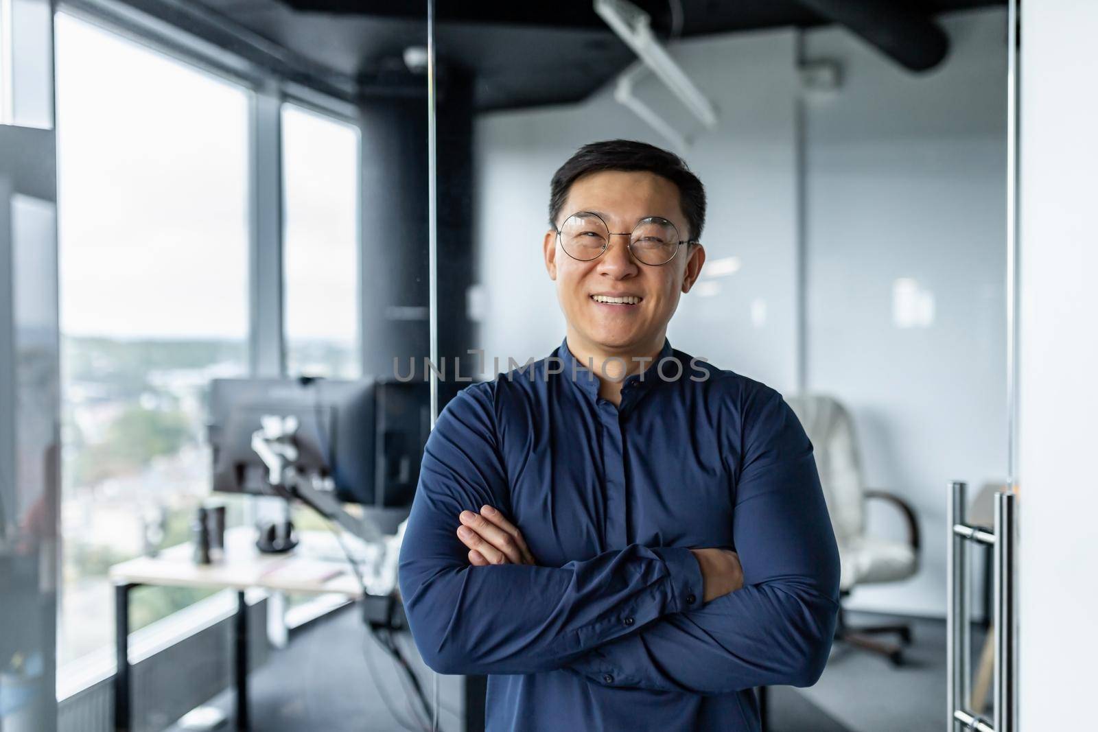 Portrait of successful asian businessman with crossed arms, businessman investor working inside office building loft, looking at camera and smiling, satisfied investor financier.