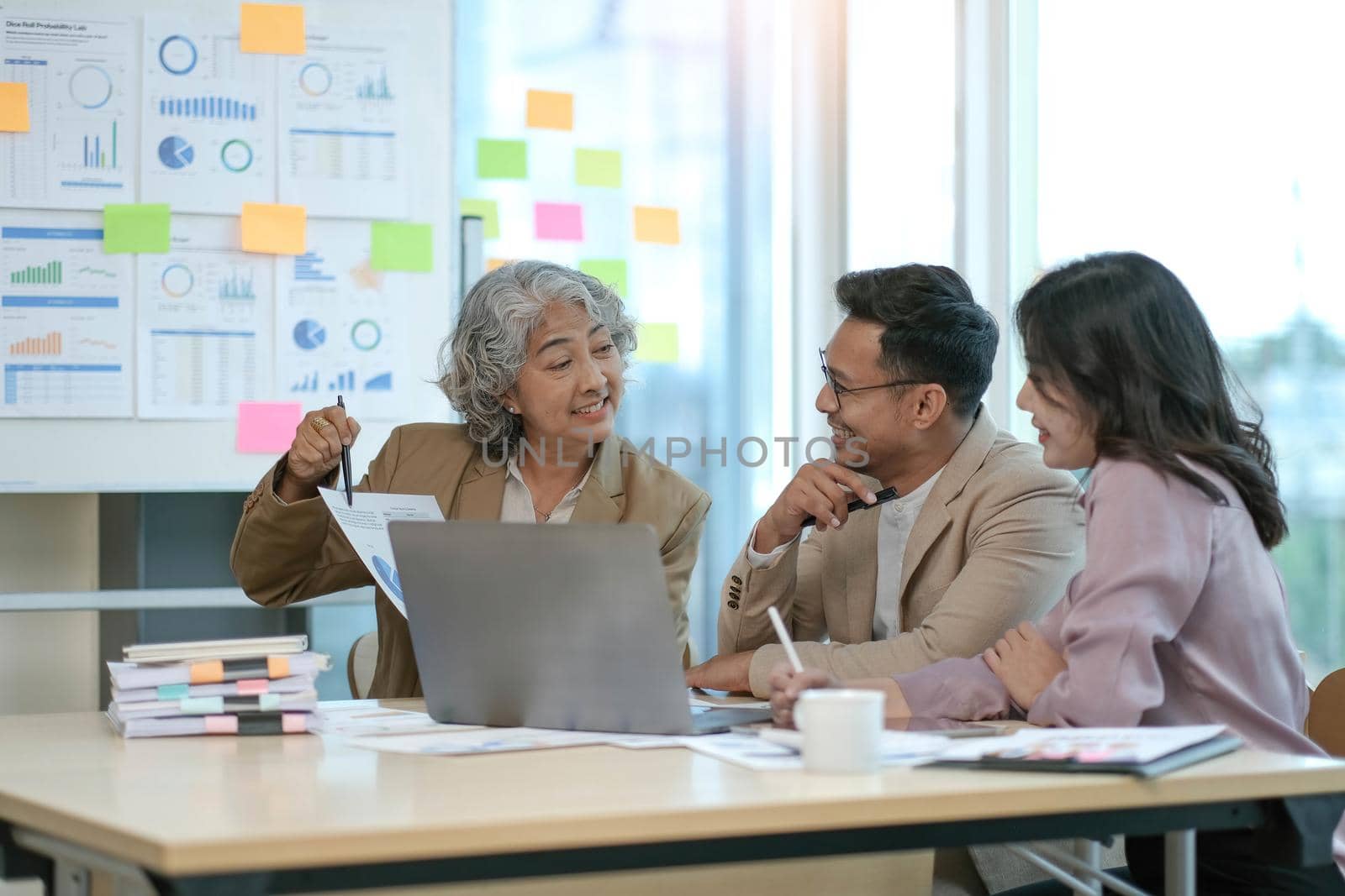 group of four happy young asian corporate executives working together meeting in office discussing business in office. by wichayada