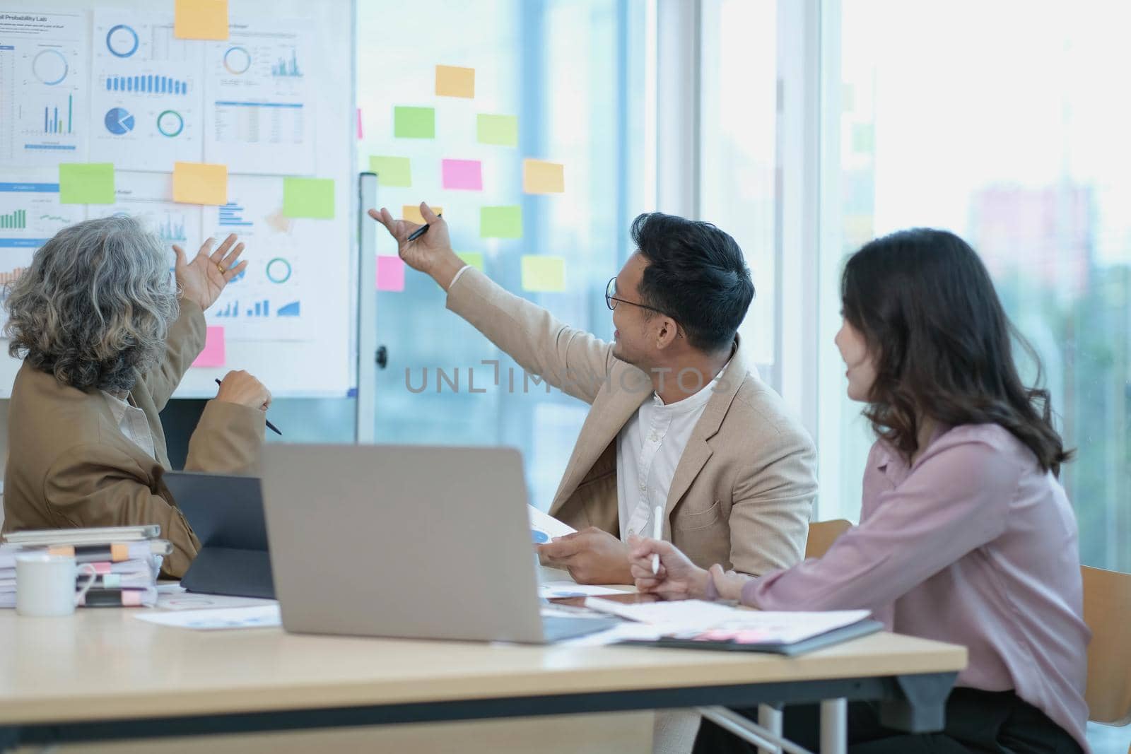 Group of Asian business people discuss together in team brainstorm meeting, work late night in office. Corporate business, coworker teamwork, financial consultant, or young entrepreneur concept.