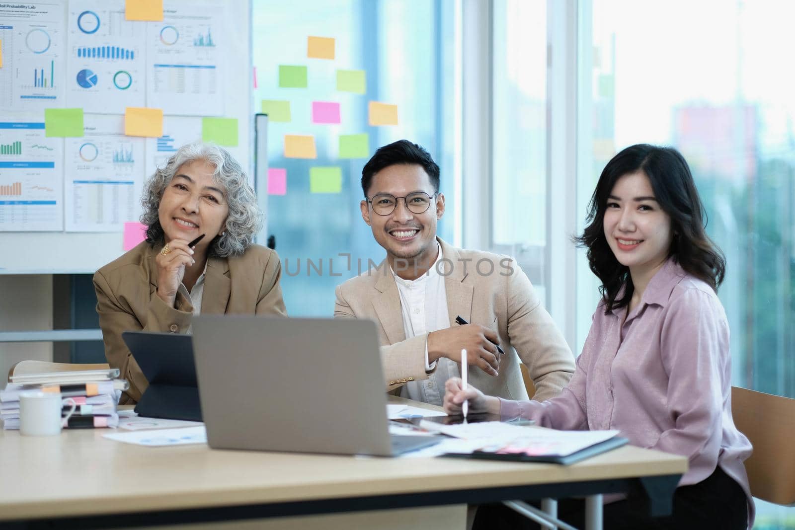 Group of Asia young creative people in smart casual wear smiling in creative office workplace. Diverse Asian male and female stand together at startup. Coworker teamwork concept. by wichayada