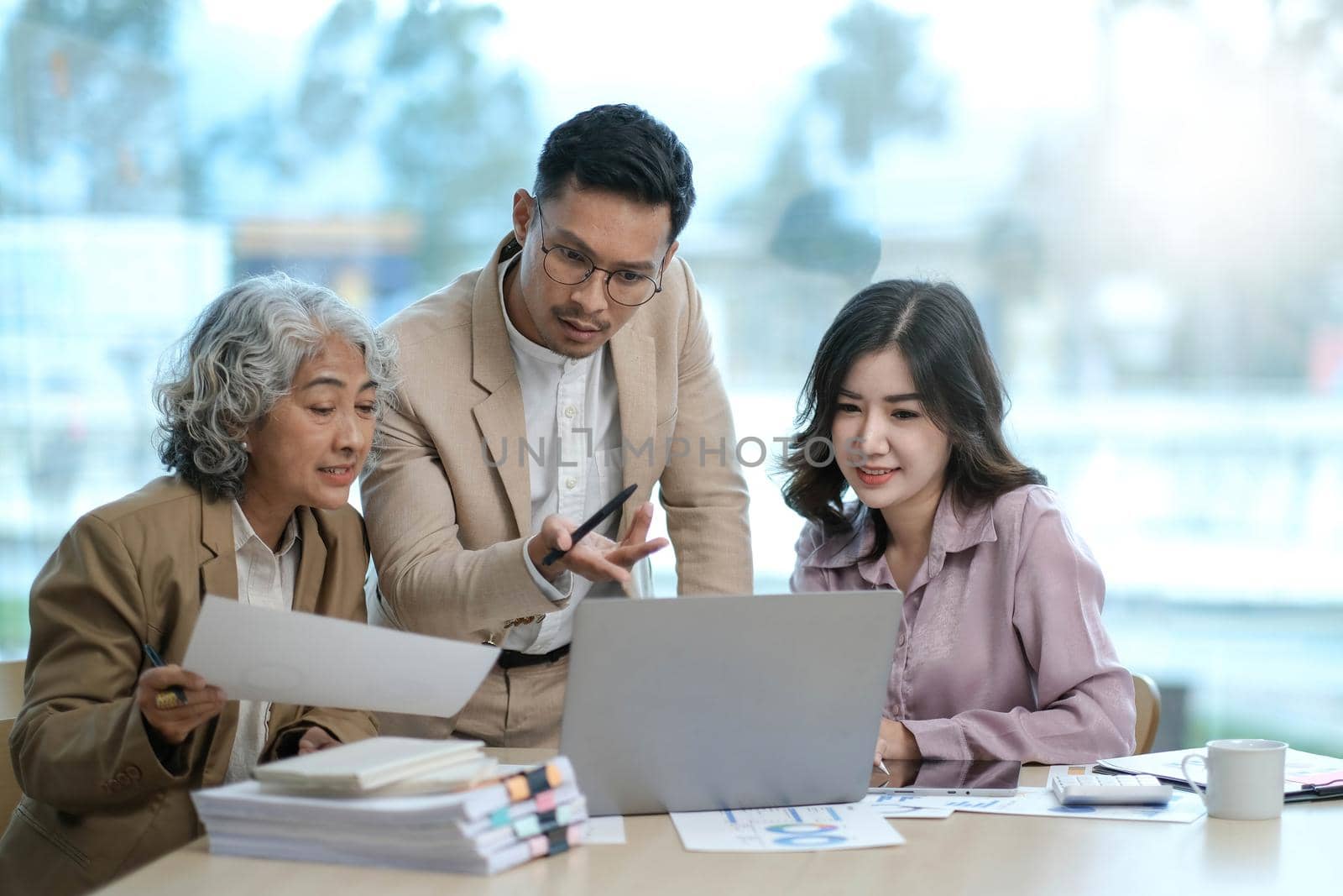 group of four happy young asian corporate executives working together meeting in office discussing business in office. by wichayada