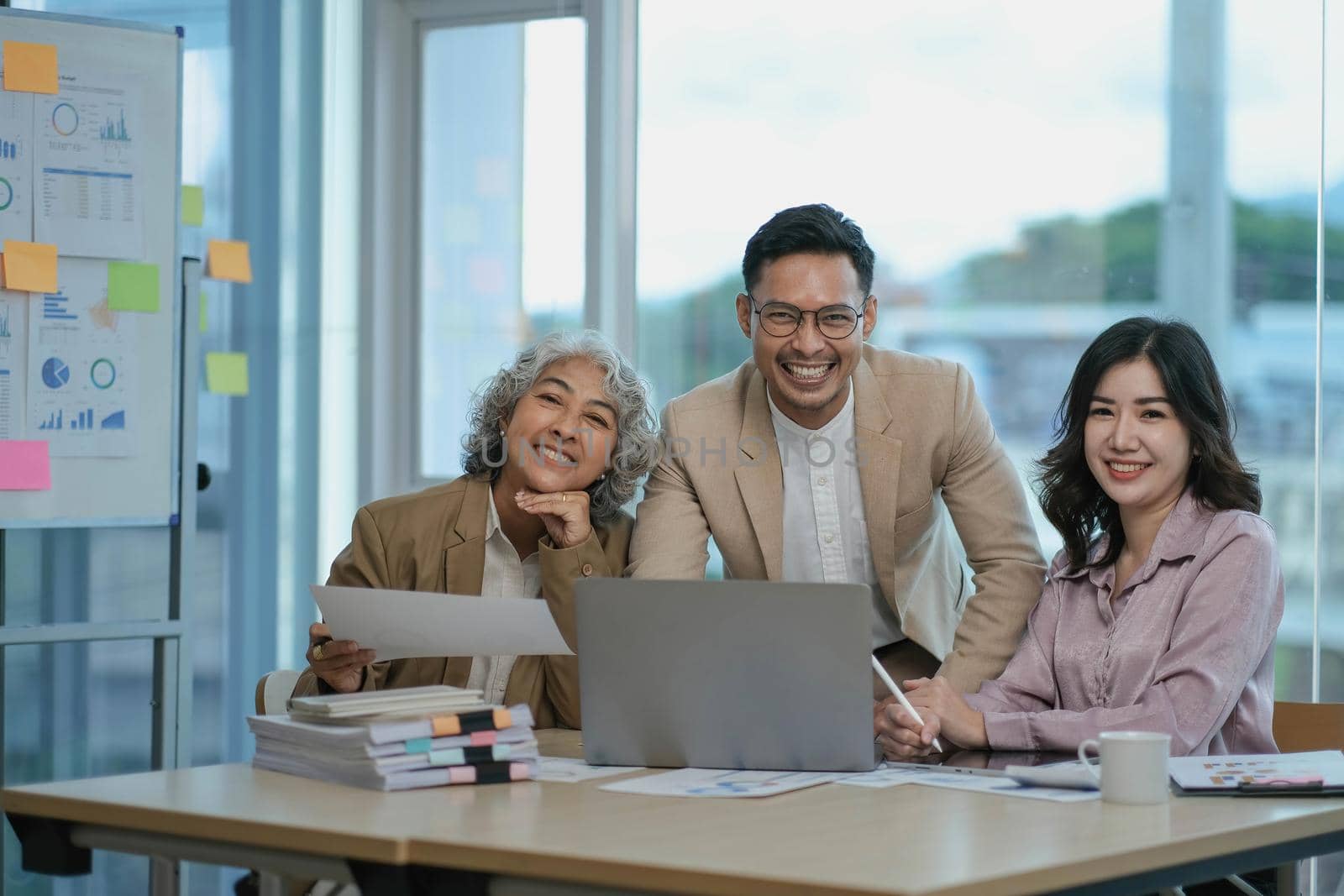 Group of Asia young creative people in smart casual wear smiling in creative office workplace. Diverse Asian male and female stand together at startup. Coworker teamwork concept. by wichayada